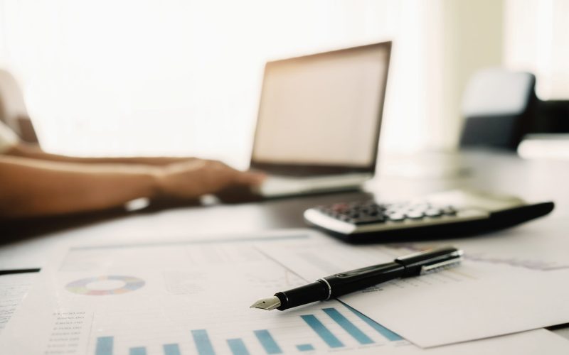 Business concept with copy space. Office desk table with pen focus and analysis chart, computer, notebook, cup of coffee on desk.Vintage tone Retro filter, selective focus.