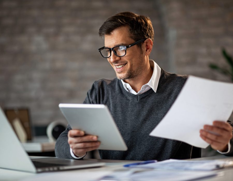 Happy businessman using touchpad and laptop while working on business reports in the office.