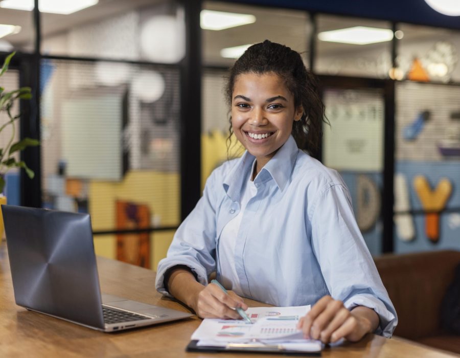 mulher-sorridente-trabalhando-com-laptop-e-papeis-no-escritorio